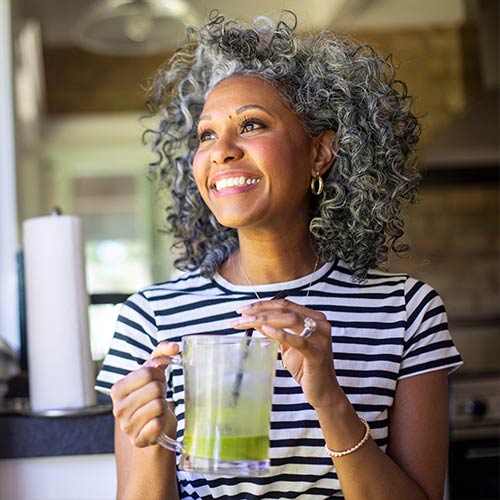 A woman smiling holding a green smoothie