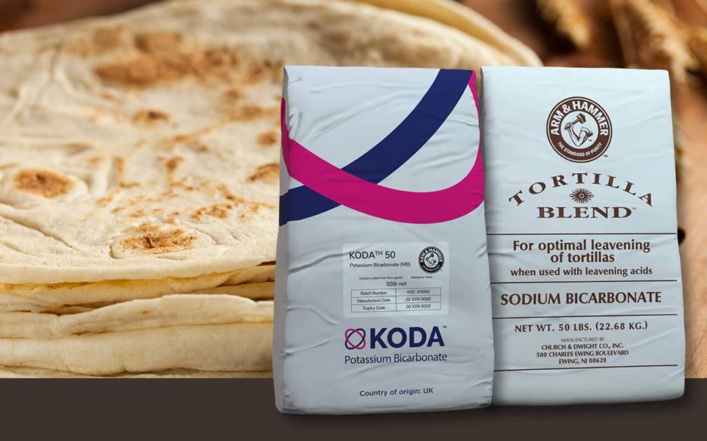 Bags of Kudos KODA™ 50 Potassium Bicarbonate and ARM & HAMMER™ TORTILLA BLEND™ Sodium Bicarbonate in foreground with golden brown tortilla stack with wheat in background